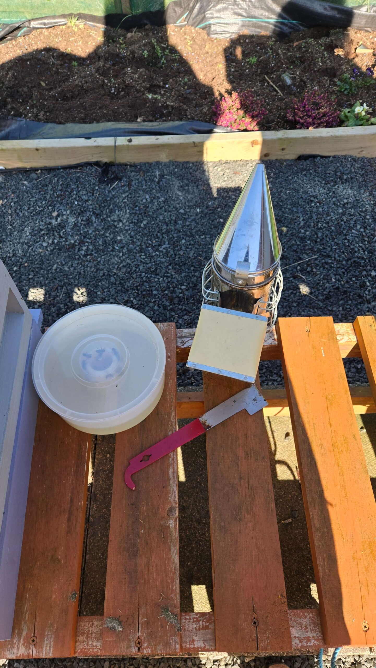 Smoker, hive tool and feeder laid out on the hive stand. The smoker is not optional.