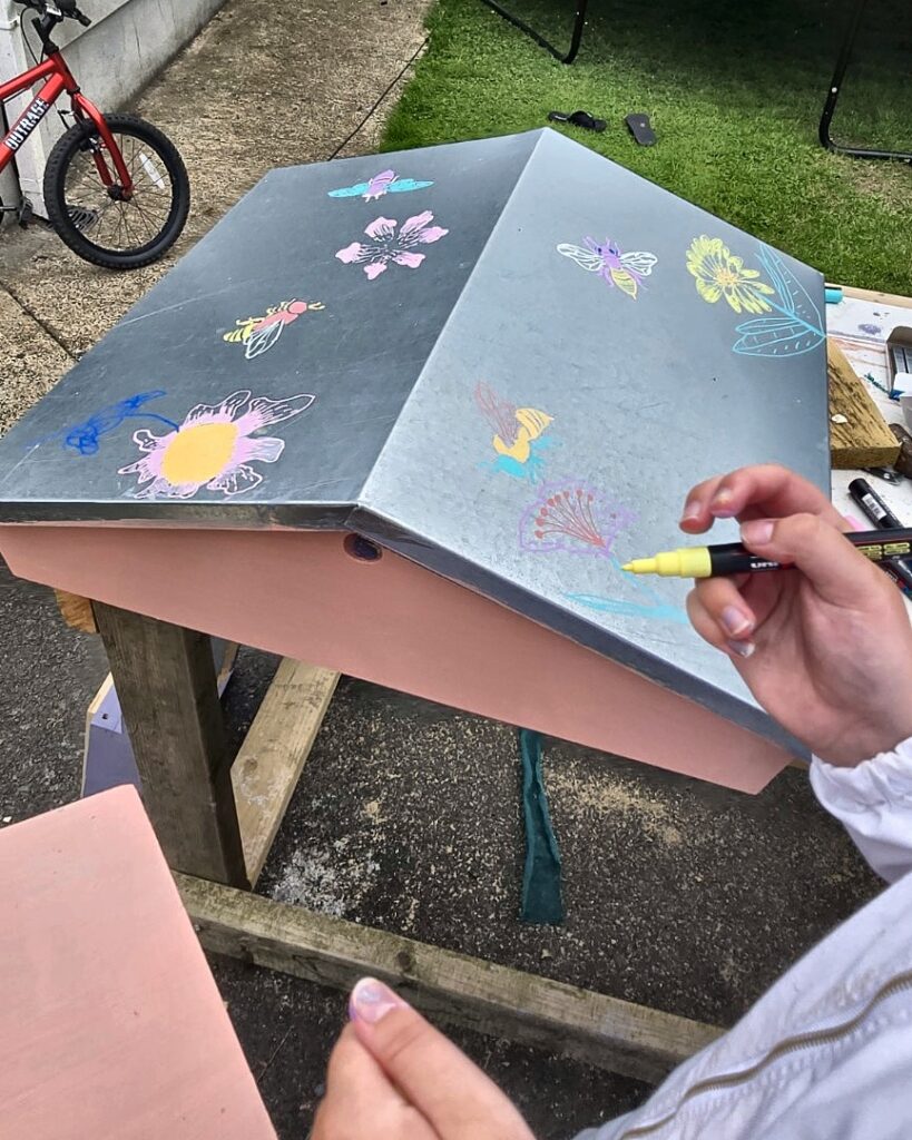 Bee Girl drawing bees and flowers in chalk on the hive roof.