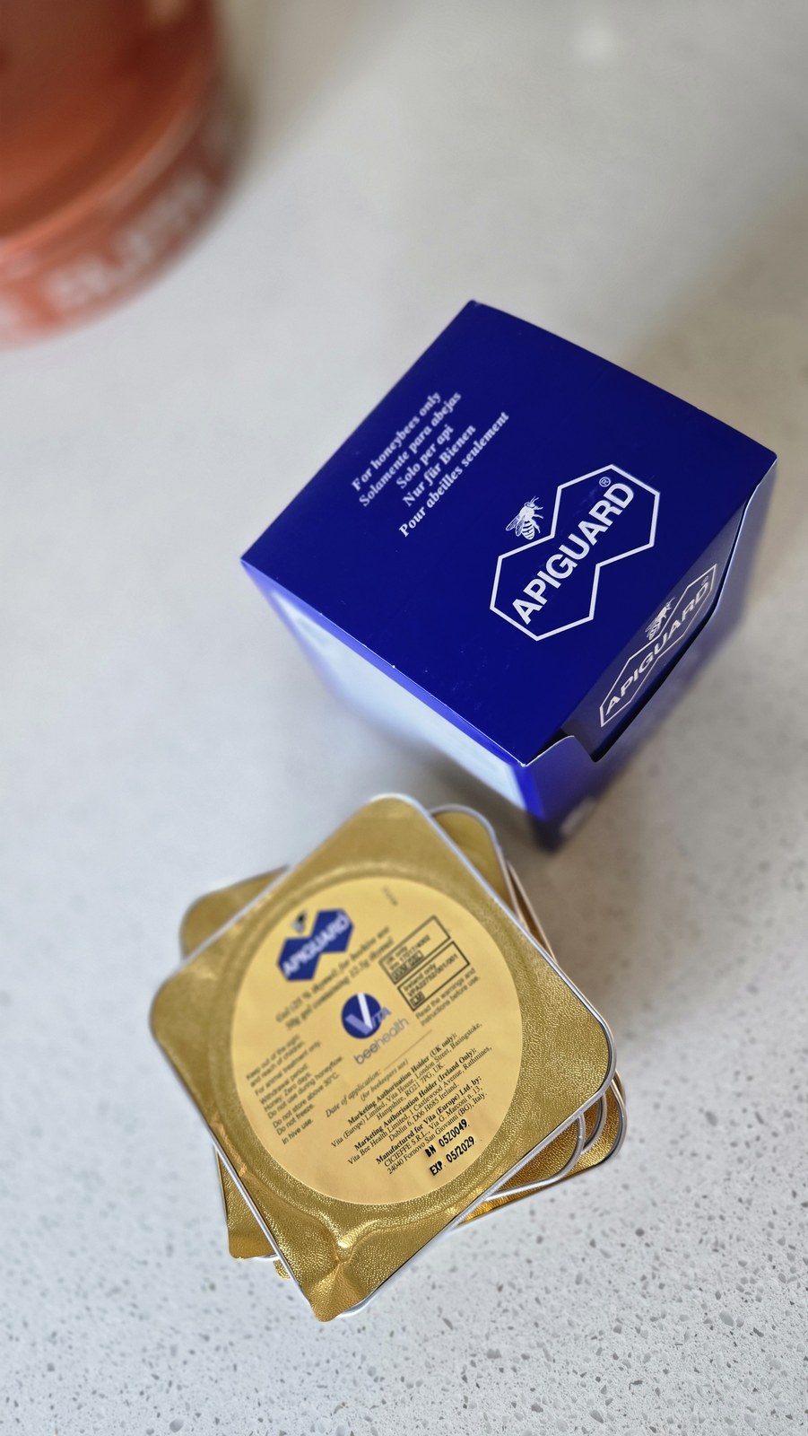 The blue Apiguard box beside a stack of gold foil treatment trays on a kitchen counter
